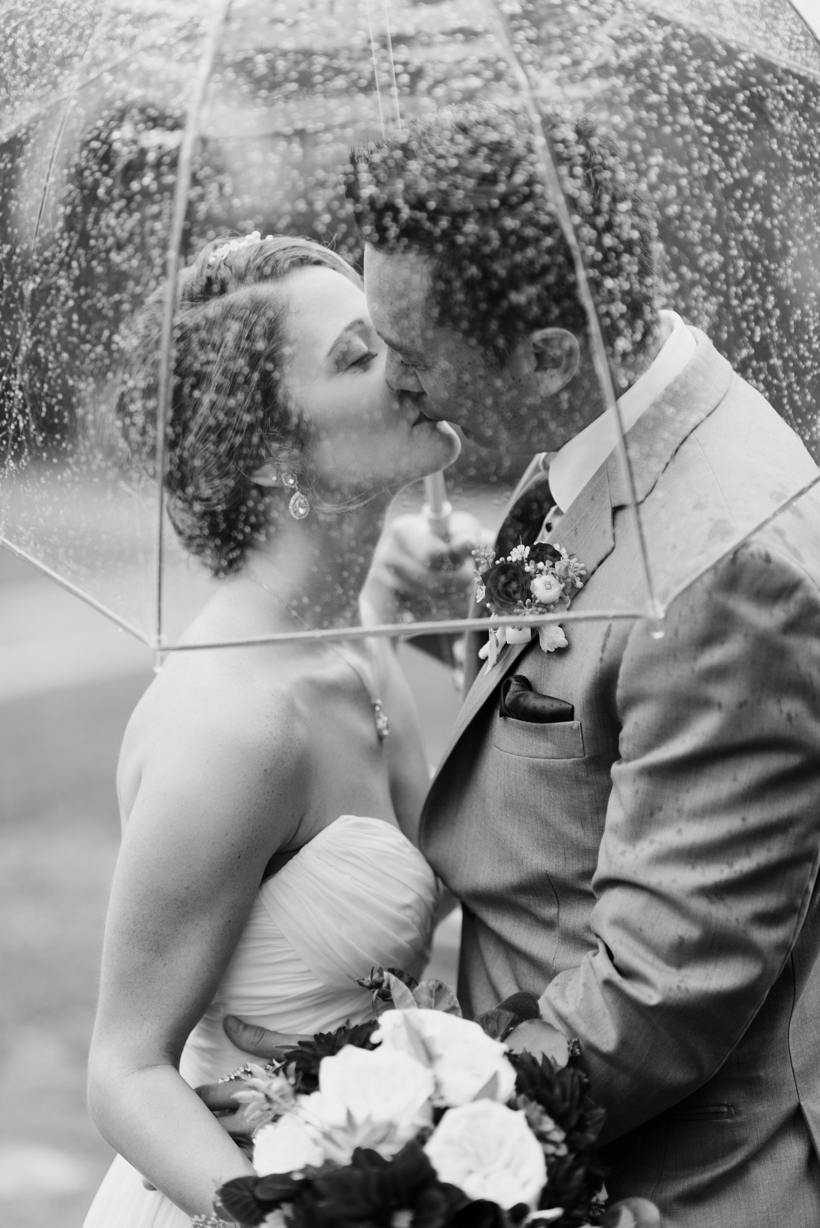 black and white of couple kissing under umbrella on wedding day